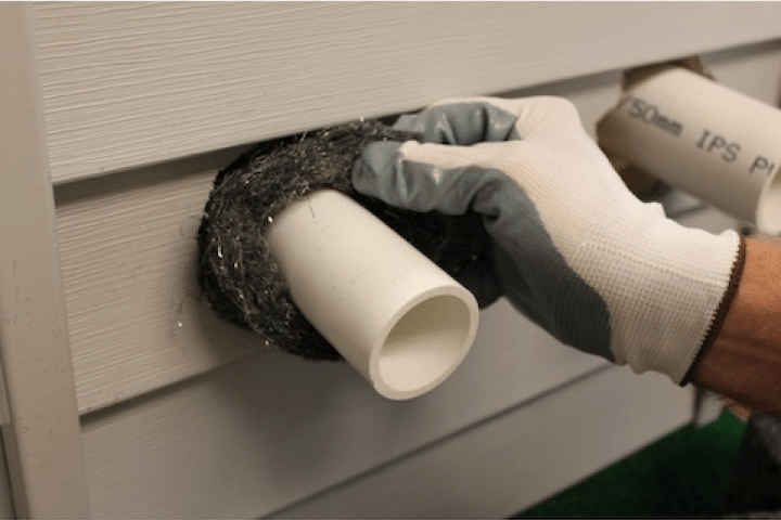 Crawl Pros professional installing a rodent exclusion on pipes outside of a home