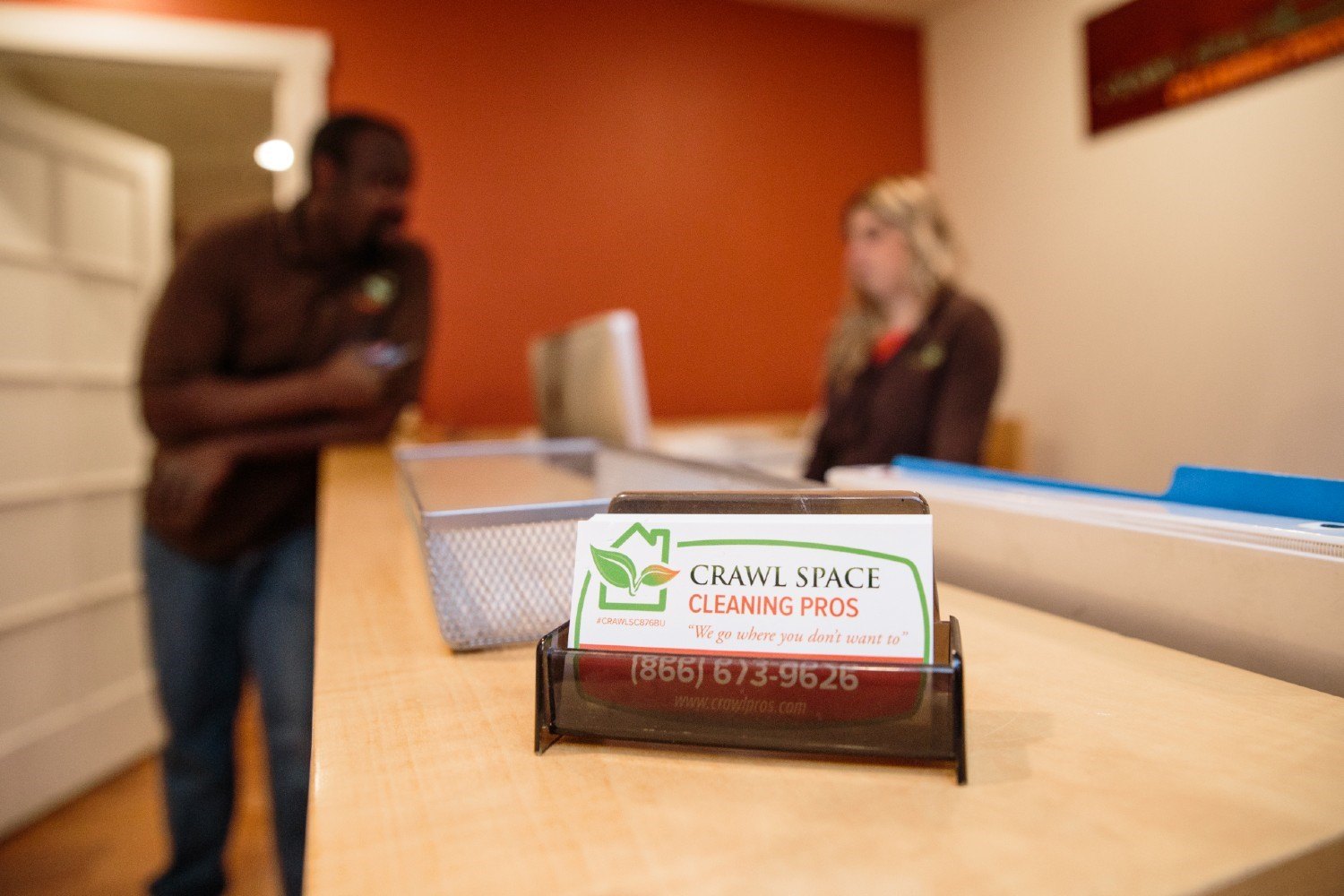 Crawl Pros business card sitting on. a desk with two employees talking in the background